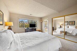 A bedroom with a large bed, a television, a dresser, and a mirror. - Beautiful Desert Falls Country Club Upper Unit Condo (Palm Desert)