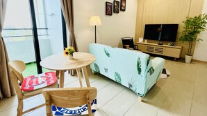 Een moderne woonkamer met een bank, een televisie, een klein tafeltje met een lamp en een stoel met een kussen.