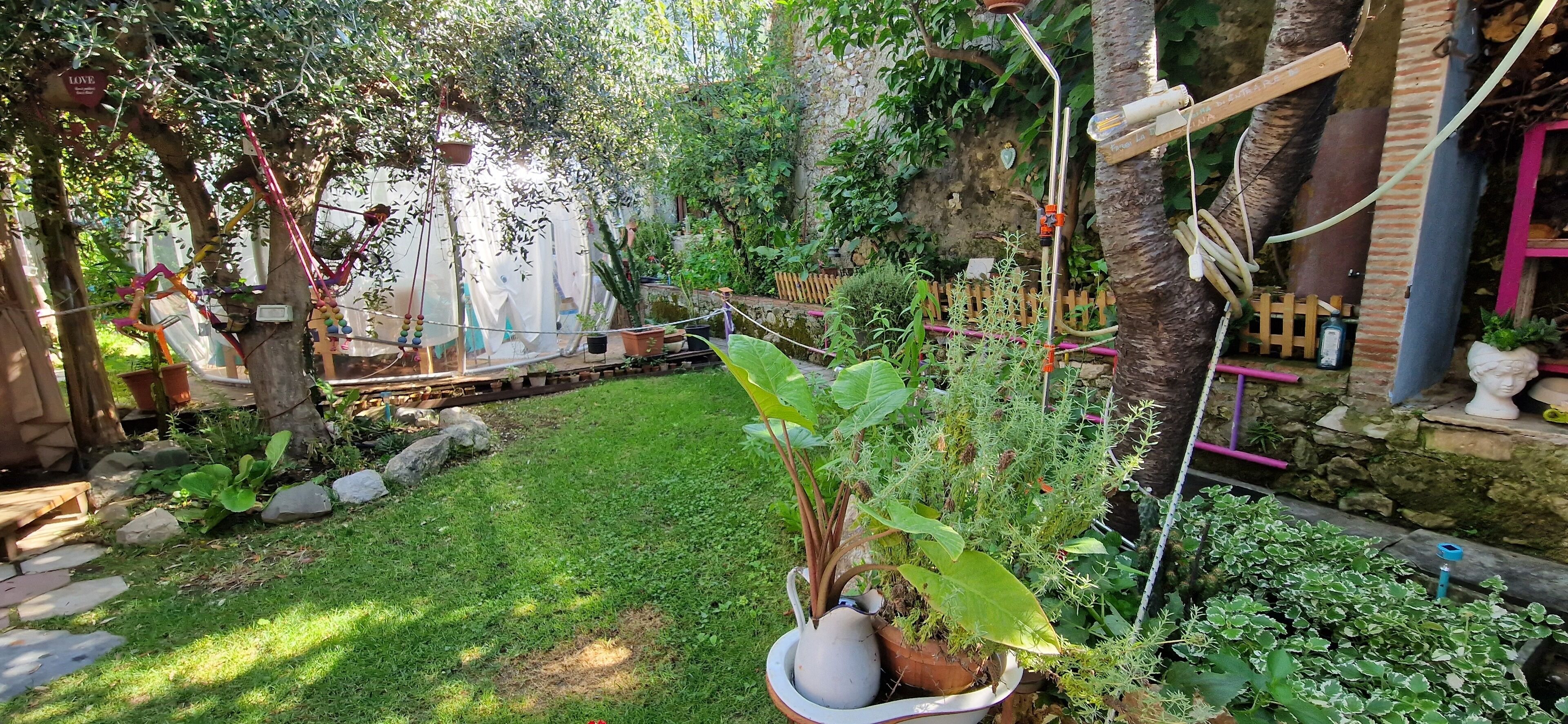 Un jardin avec une pelouse, des plantes en pot, une clôture en bois et un mur de pierre.