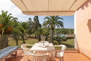 A balcony with a table, chairs, and a bench, overlooking a pool and palm trees. - Classical Residence Baia delle Palme Premium Bilo 4 sleeps 4 (Santa Margherita di Pula)