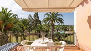 A balcony with a table, chairs, and a bench, overlooking a pool and palm trees.