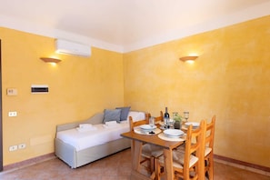 A compact room with a bed, a dining table with chairs, and a wall-mounted air conditioner. - Classical Residence Baia delle Palme Premium Bilo 4 nm1213 (Santa Margherita di Pula)