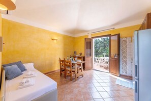 A room with a bed, a dining table, chairs, a refrigerator, and a sliding glass door leading to an outdoor area.