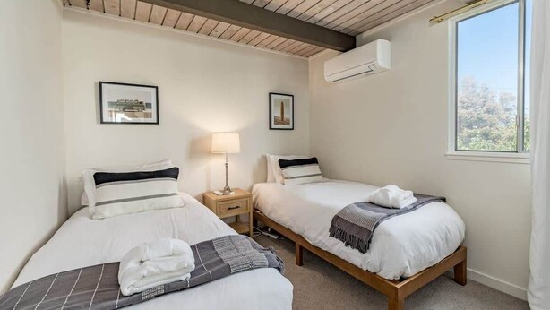 A hotel room with two beds, a nightstand, a lamp, and a window with a view.