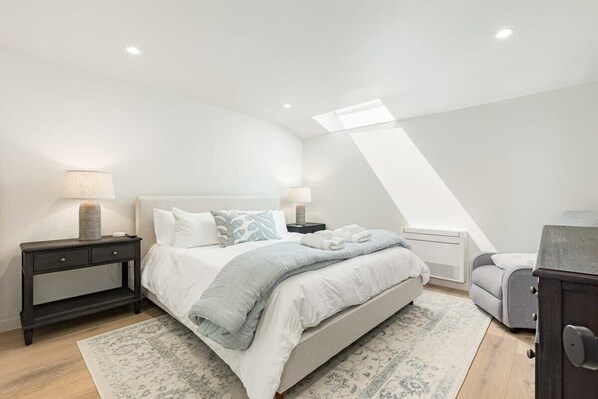 A bedroom with a bed, nightstands, a dresser, and a skylight.