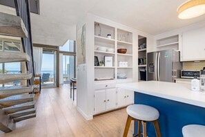 A modern kitchen with white cabinetry, a blue island, and a view to the outside.