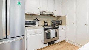 A kitchen with white cabinets, a stainless steel refrigerator, a microwave, a kettle, and an oven.