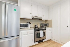 A compact kitchen with white cabinets, a stainless steel refrigerator, a microwave, a kettle, and an oven. - Stunning Oceanfront - Sunset Magazine Home (Santa Cruz)