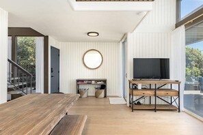 A modern living room with a wooden table, a TV on a wooden stand, and a staircase leading to an outdoor area.