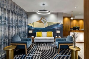 Moderni hotellihuone, jossa on sänky, kaksi nojatuolia, työpöytä ja geometrisesti kuvioitu seinä.