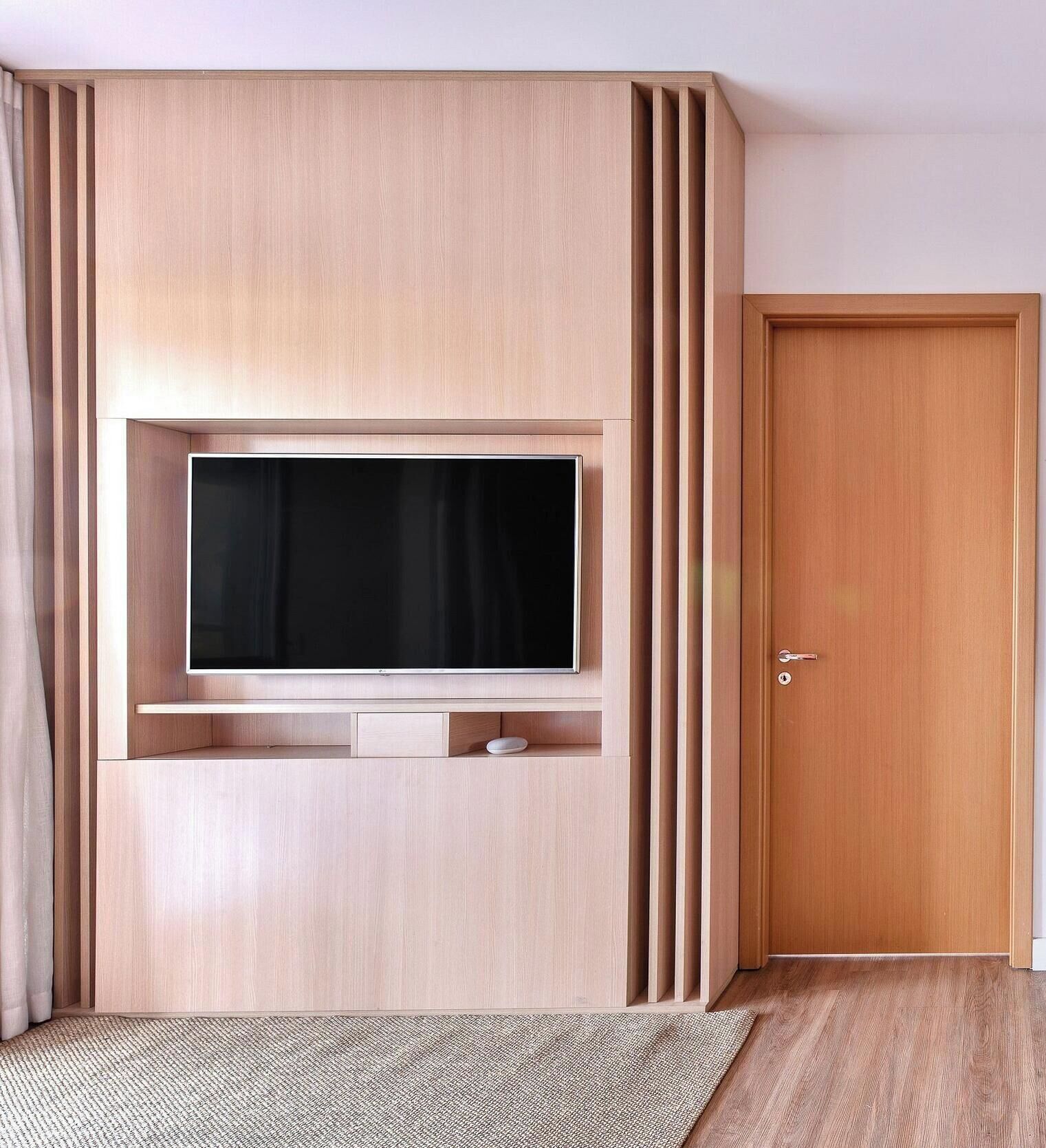 A room with a built-in TV, a wooden door, and a patterned rug.