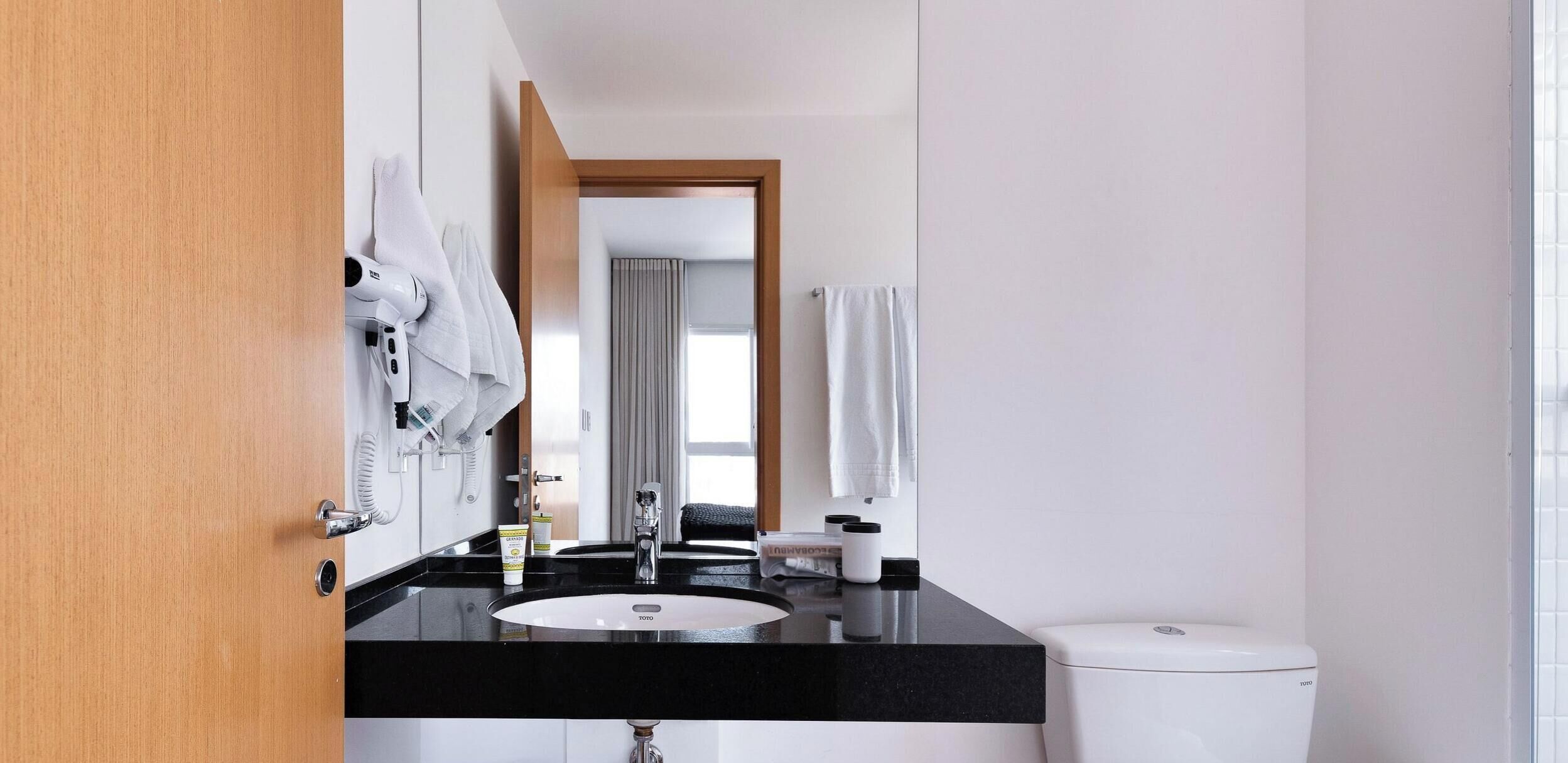Une salle de bain moderne avec un plan de toilette noir, un lavabo blanc et des toilettes de la marque Toto.