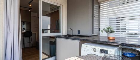 A modern kitchen with a built-in dishwasher, a dining area with a table and chairs, and a sliding glass door leading to a balcony.