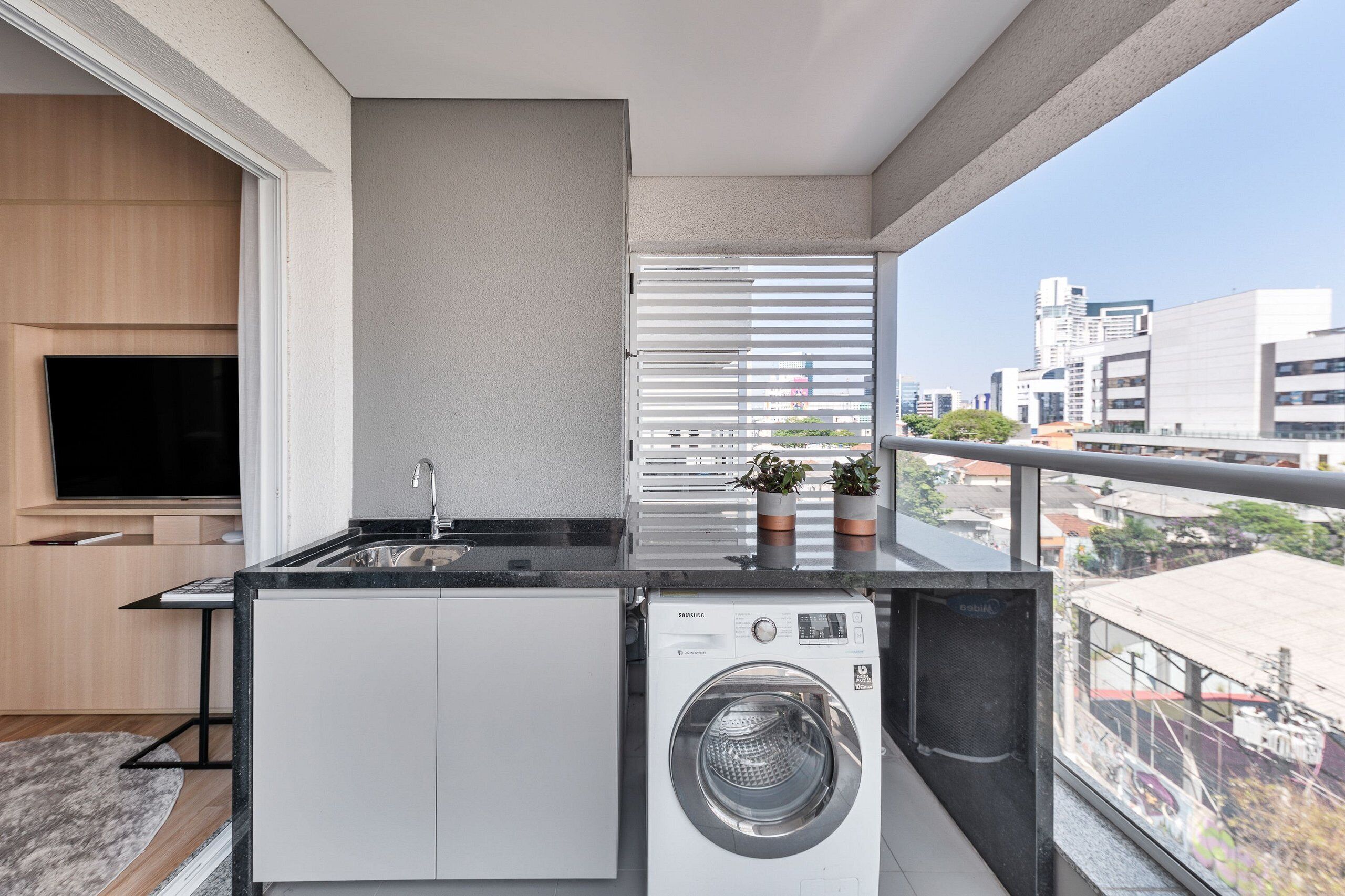 A compact kitchen with a washing machine, a TV, and a balcony with a city view.