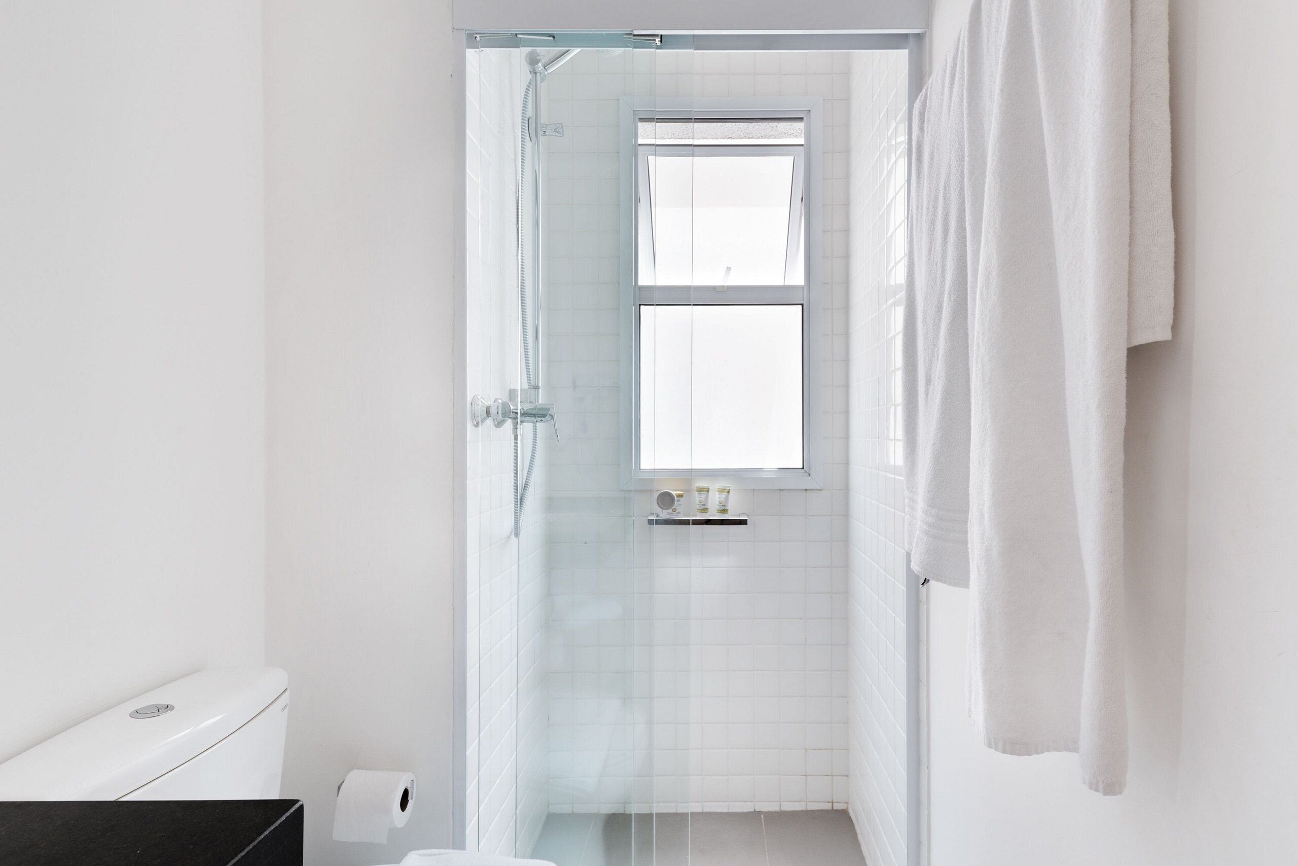 Ein Badezimmer mit Duschkabine aus Glas, Toilette und Fenster.