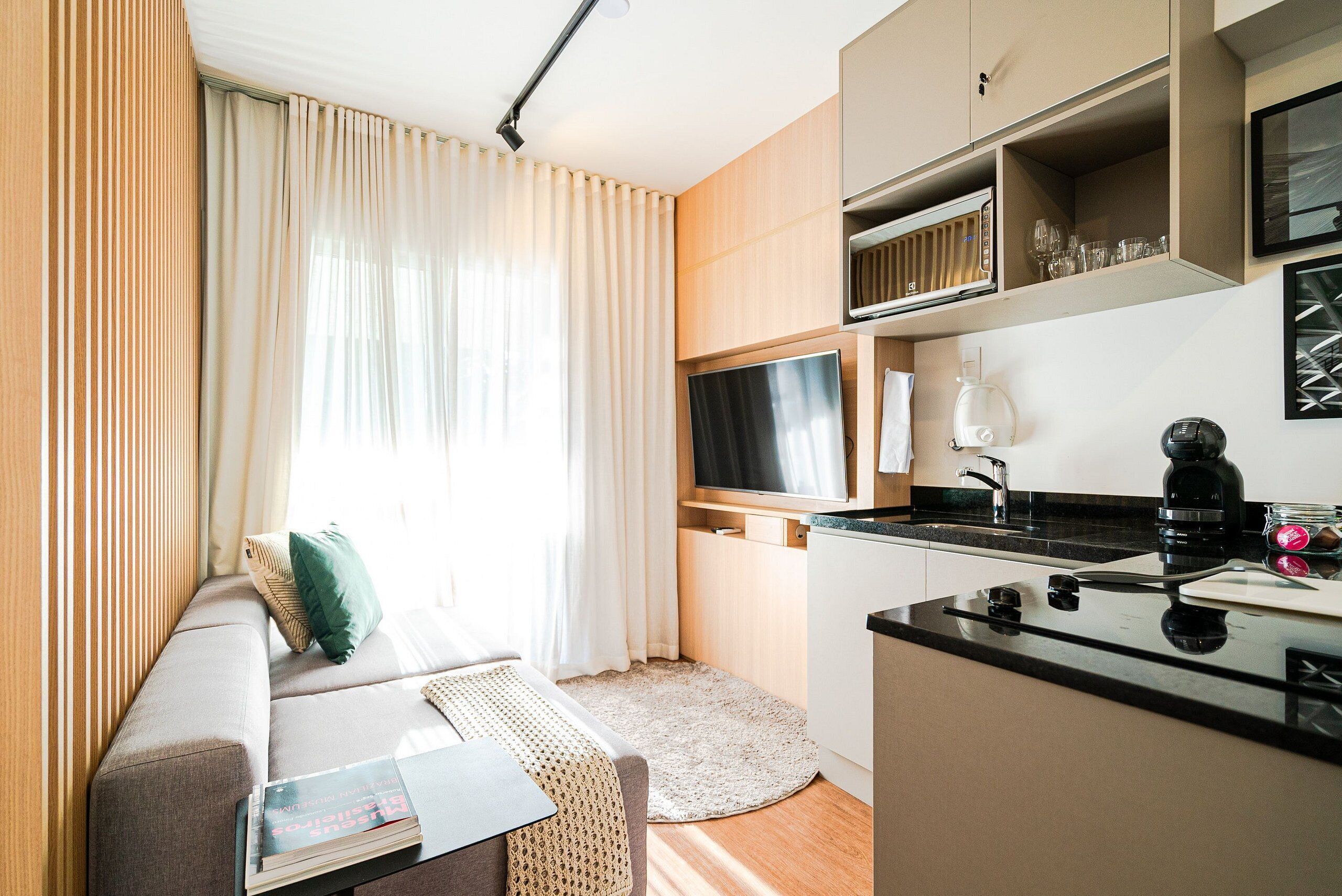 A modern room with a sofa, a flat-screen TV, a coffee maker, and a kitchen area.
