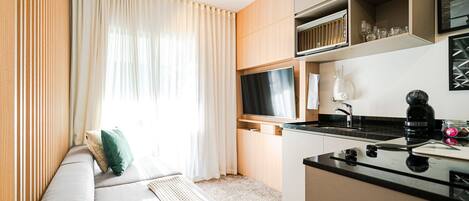 A modern room with a sofa, a flat-screen TV, a coffee maker, and a kitchen area.