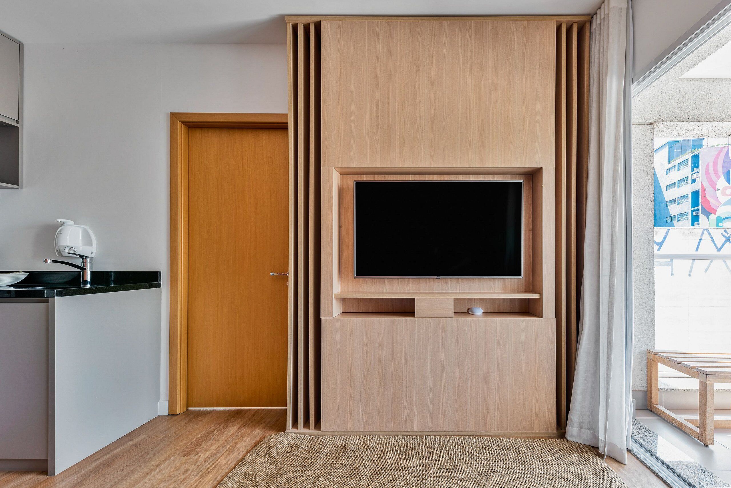 A modern room with a built-in TV, a wooden door, and a kitchen area with a kettle.