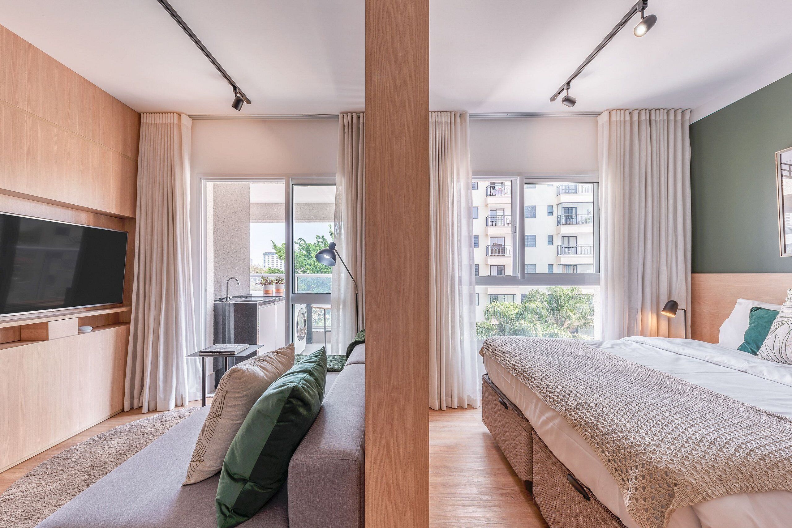 Habitación de hotel moderna con un televisor de pantalla plana grande, un sofá, una cama y un balcón con vistas a la ciudad.