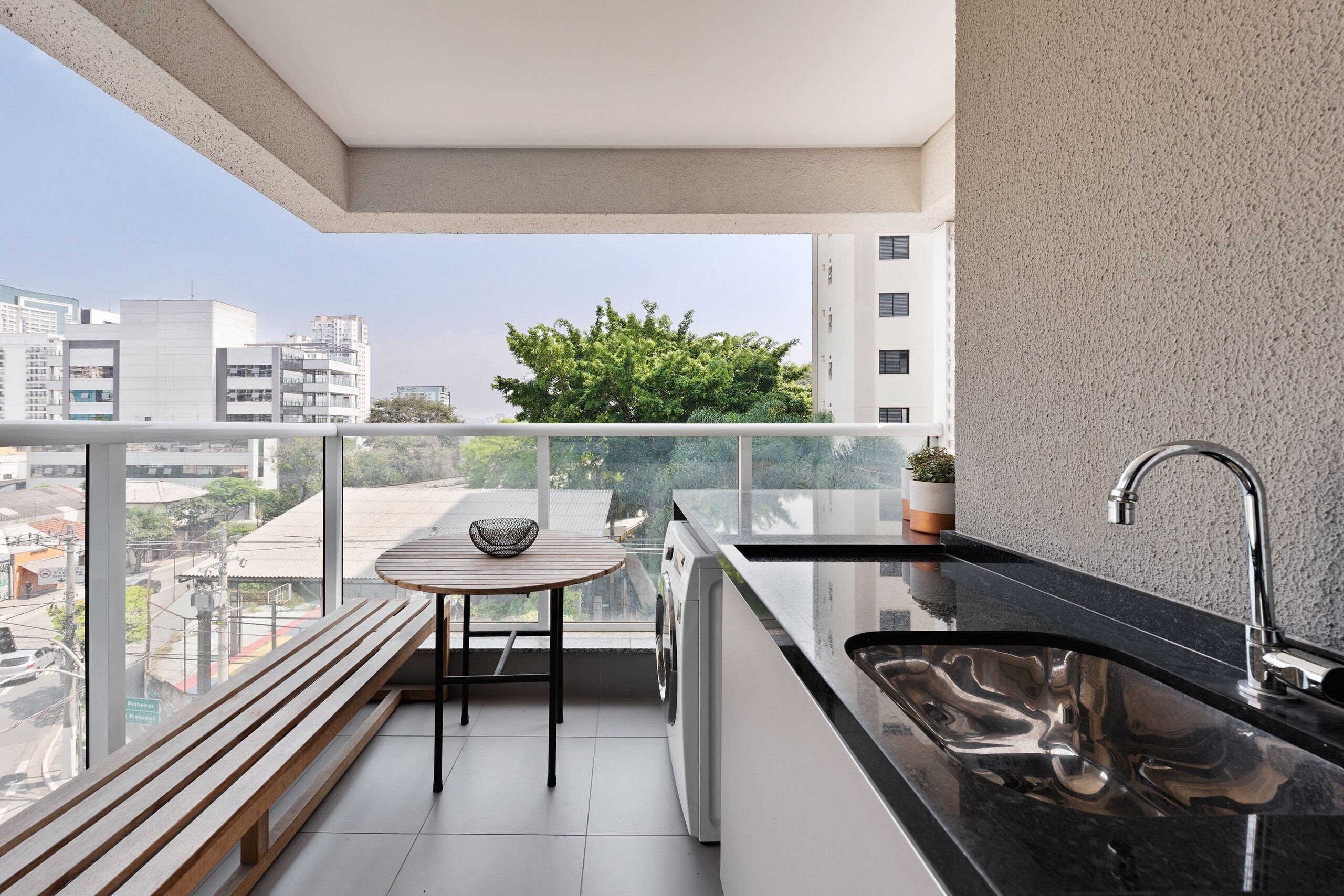 A balcony with a washing machine, a sink, and a table with a chair.