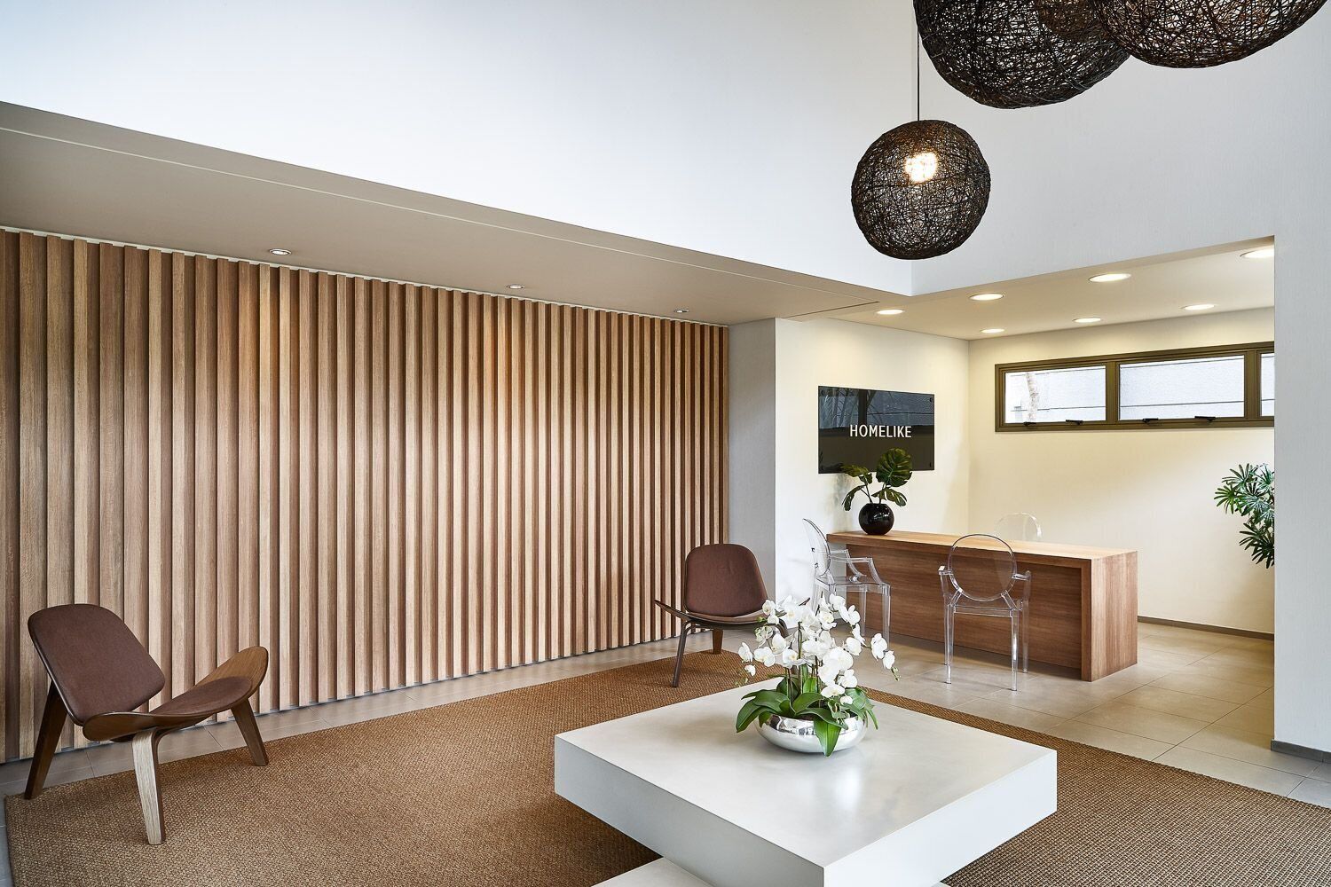 Un área de recepción moderna con un muro de listones de madera, un mostrador y dos sillas.