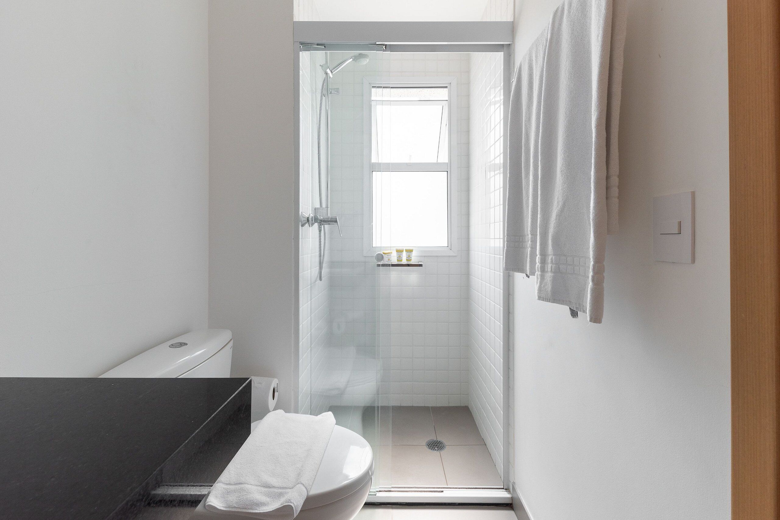 Un baño con inodoro, ducha con puerta de cristal y lavamanos con toalla.