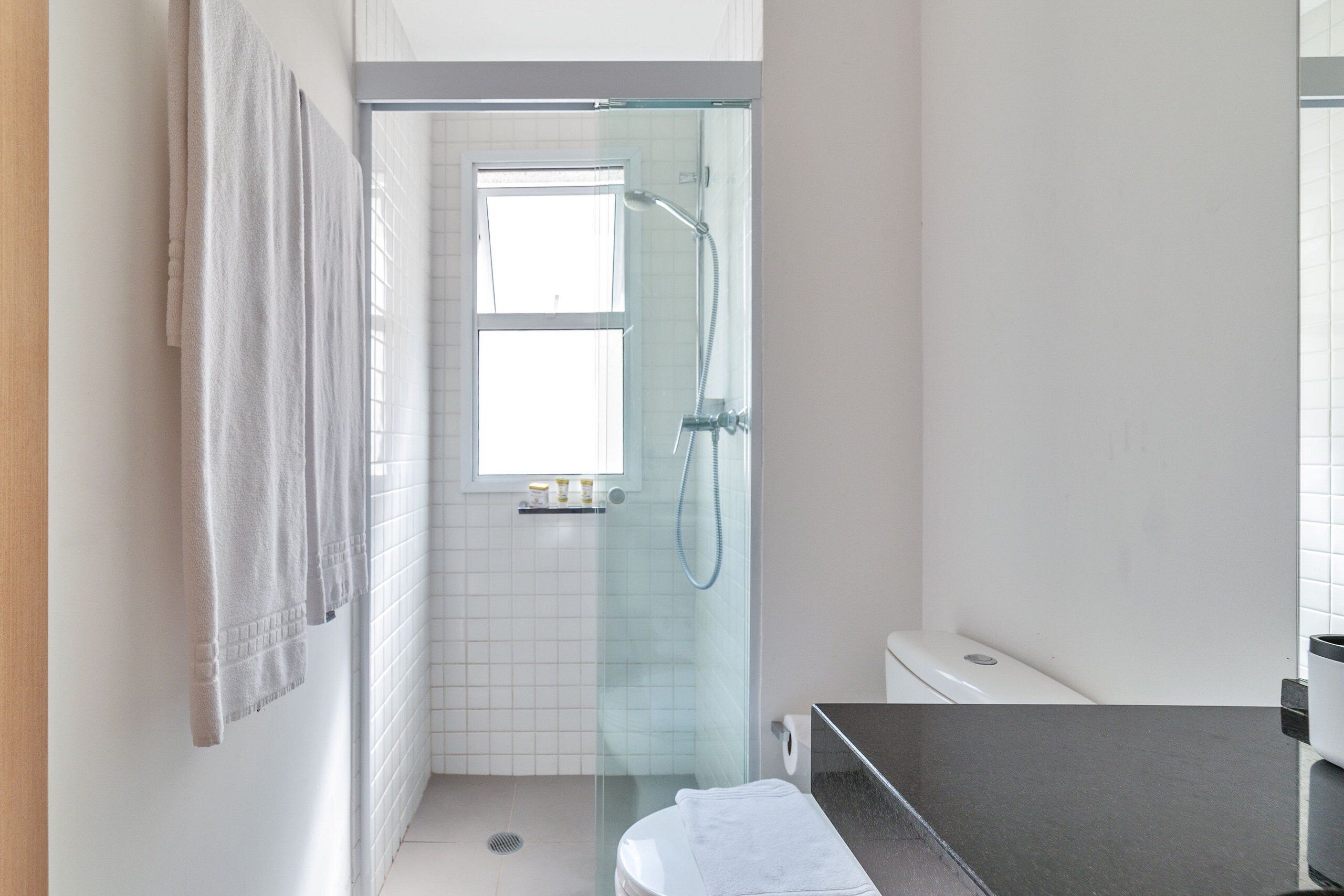 A modern bathroom with a glass-enclosed shower, white tiles, and a visible window.