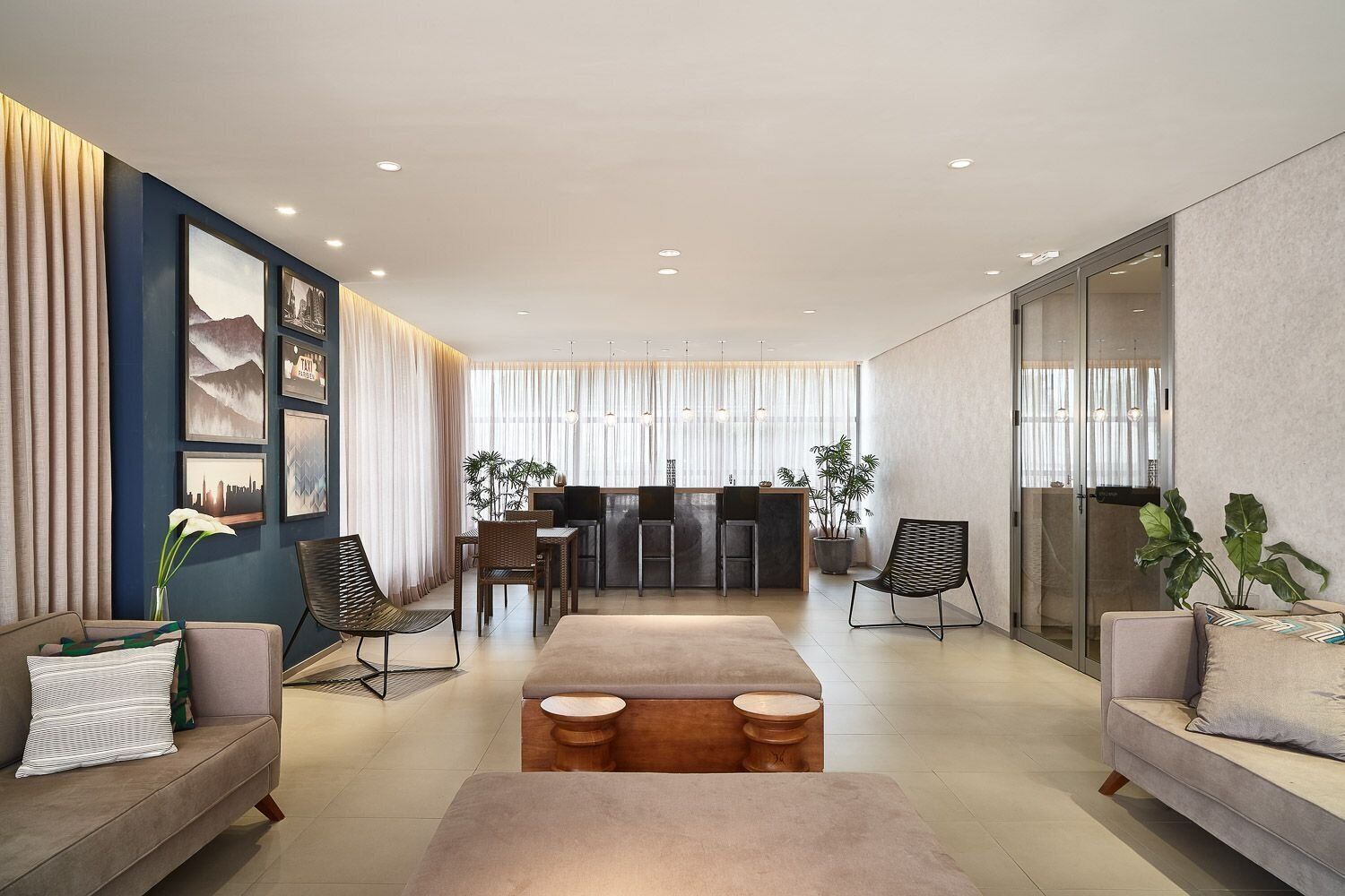 A modern living room with a sofa, a coffee table, a dining area with chairs, a kitchen area, and a large window with curtains.