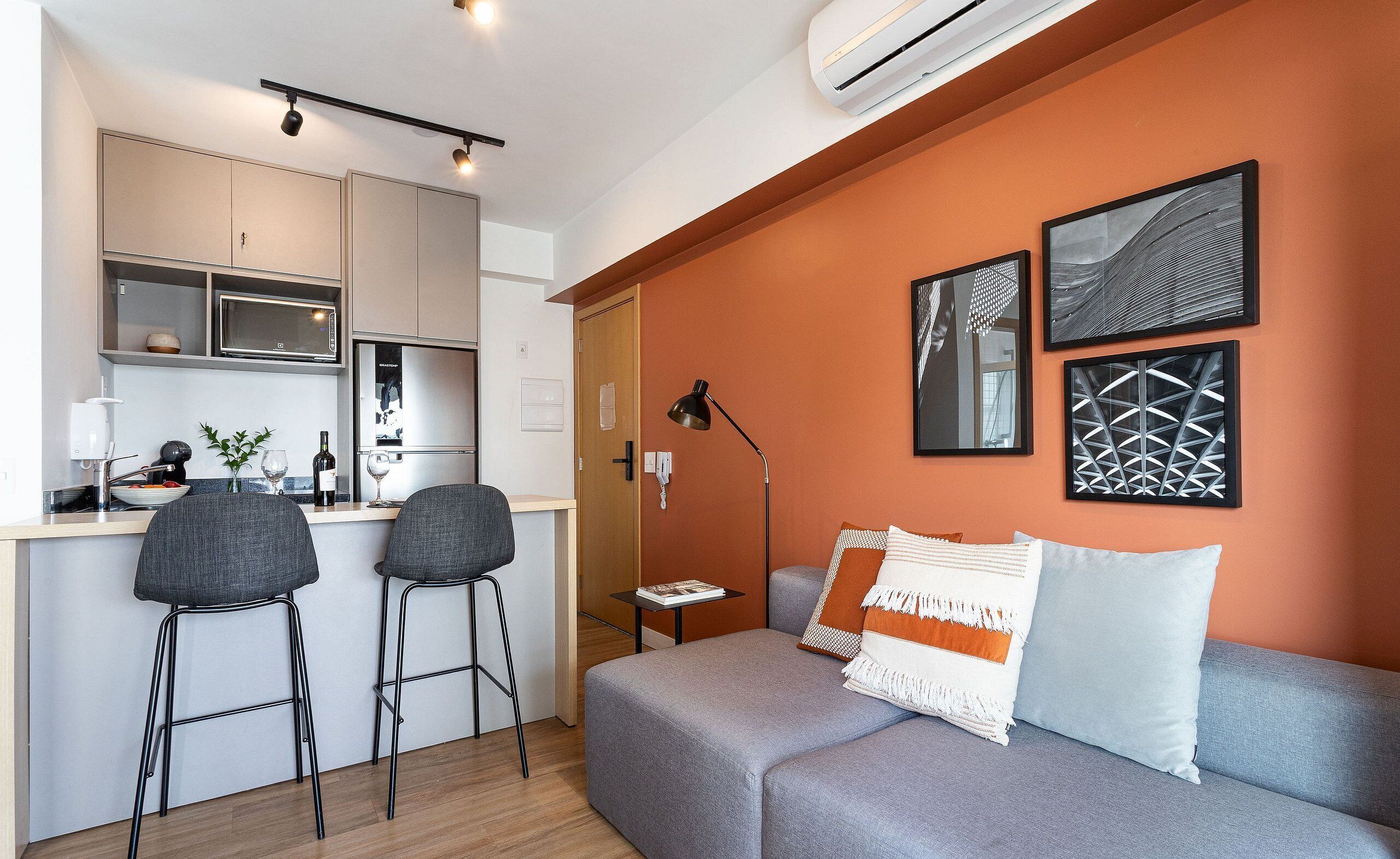 A compact living space with a kitchenette, a sofa with decorative pillows, and wall-mounted artwork.