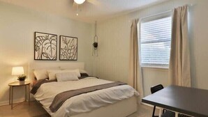Ein Schlafzimmer mit einem Bett, Nachttischen, einem Schreibtisch und einem Fenster mit Vorhängen.
