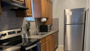 A kitchen with wooden cabinets, stainless steel appliances, and a tiled floor. - Cozy Beach Hideaway - 1 block to the beach (Jacksonville Beach)