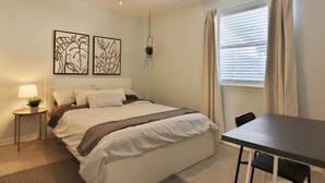 Een slaapkamer met een bed, nachtkastje, lamp en een raam met gordijnen.
