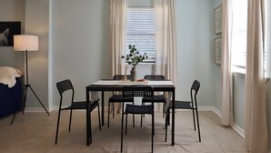 Een eetruimte met een tafel, stoelen, een plant in pot en een lamp.