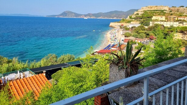 Una vista costiera con spiaggia, un edificio storico e vegetazione lussureggiante.