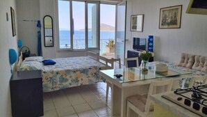A room with a bed, a dining table, a sofa, a TV, and a view of the sea.