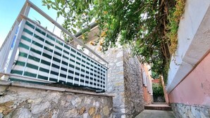 A stone staircase leading up to a building with a metal railing and a tree with green leaves.
