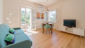 A living room with a sofa, a dining table with chairs, a TV on a stand, and a large window.