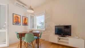 A modern living room with a wooden dining table, green chairs, a flat-screen TV, and artwork on the wall.