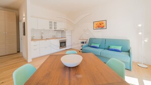 A modern apartment with a wooden dining table, a blue sofa, and a kitchen with white cabinets.