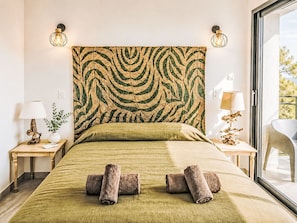 A bed with a patterned headboard, two bedside lamps, a bedside table with a lamp, and a window with a view.