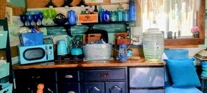 Cozinha com micro-ondas, chaleira e cafeteira no balcão, bebedouro e prateleira com recipientes de vidro e uma caixa com a etiqueta 'SAPORI DITALIA'.