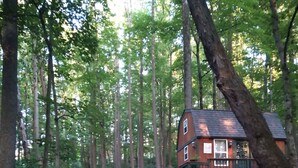 A rustic cabin with a wooden deck and a small staircase leading to a second-story balcony.