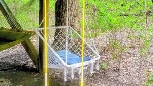 A hammock under a wooden structure with a blue and white striped mat on the ground.