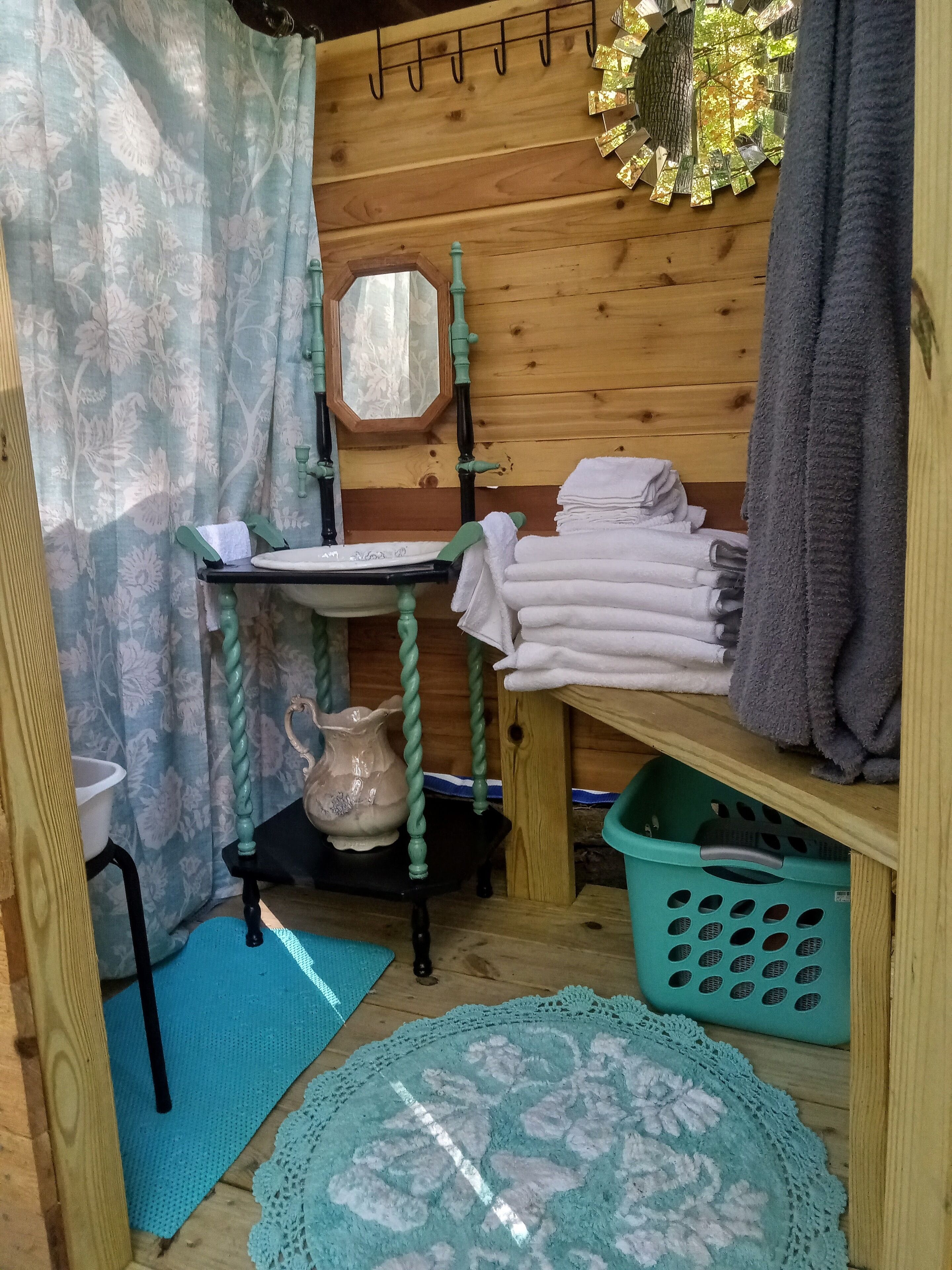 A small, cozy bathroom with wooden walls, a wooden sink, a mirror, a towel rack, a green basket, and a blue mat.