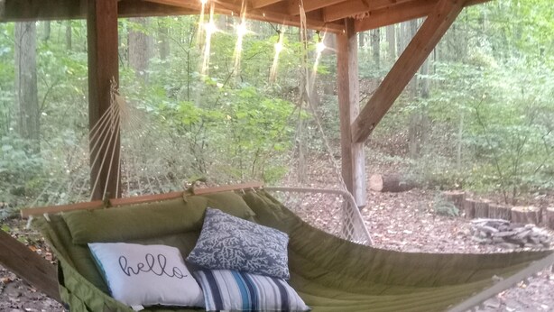 A hammock bed with pillows, hanging lights, and a view of a forest.