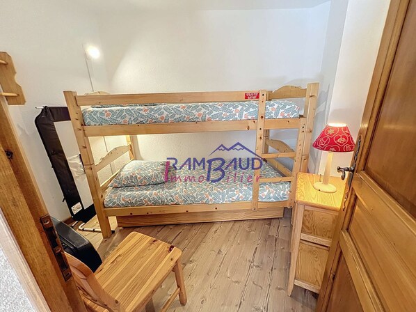 Ein Etagenbett mit blumenmusterbezogener Matratze, ein kleiner Holztisch und eine rote Lampe auf einem Nachttisch.