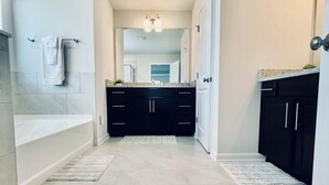 A modern bathroom with a bathtub, a towel rack, and a mirror. - Newly constructed 6 bedroom home (Frederick)
