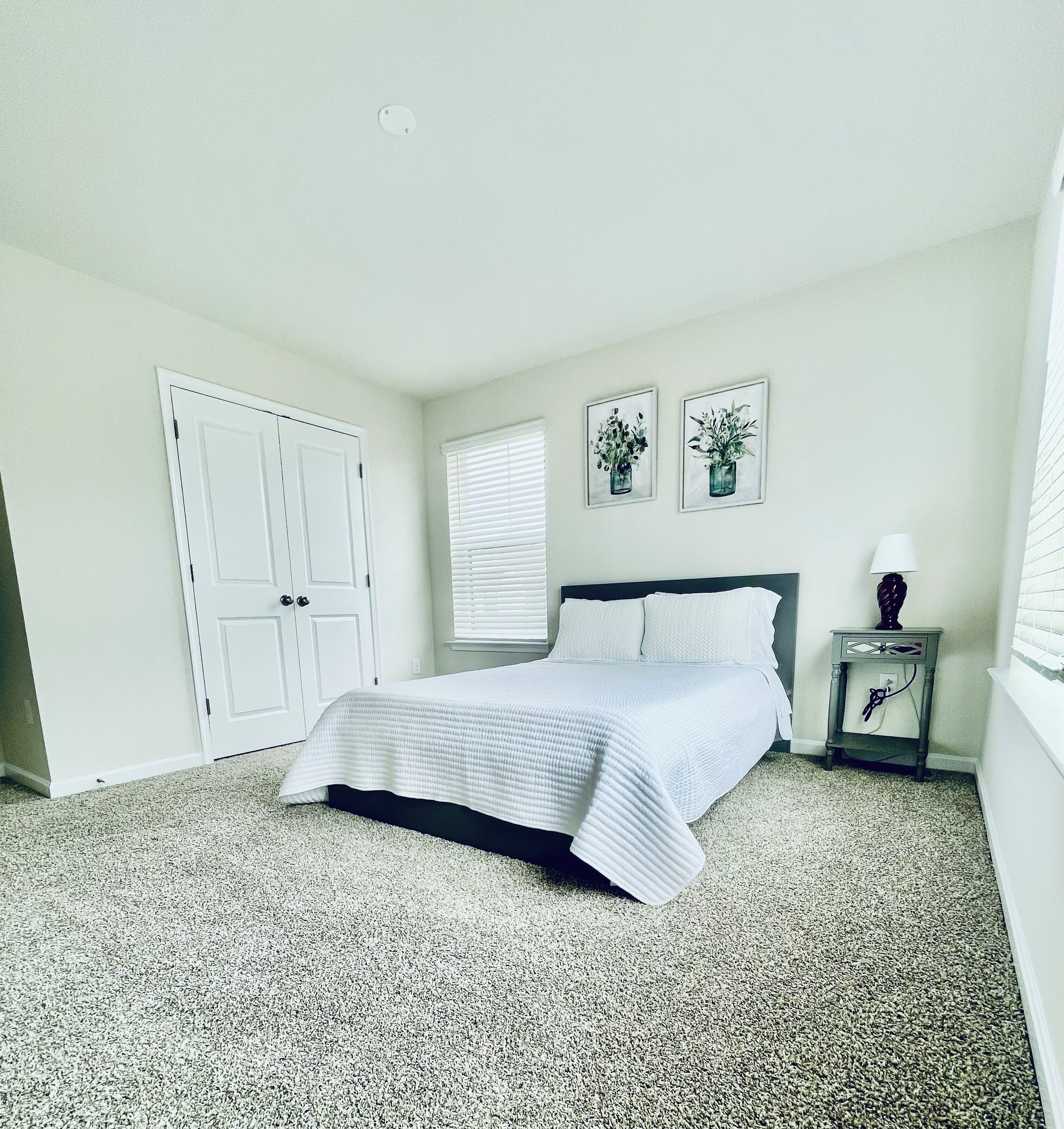 A bedroom with a bed, a nightstand, a lamp, and two wall-mounted pictures.
