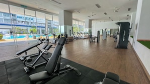 Een sportschool met trainingsapparatuur, grote ramen en uitzicht op een zwembad.