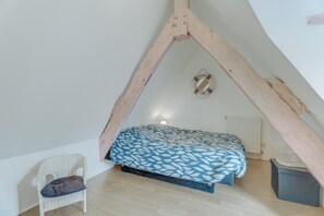 A bedroom with a sloped ceiling, a bed with a patterned bedspread, a chair, and a radiator.
